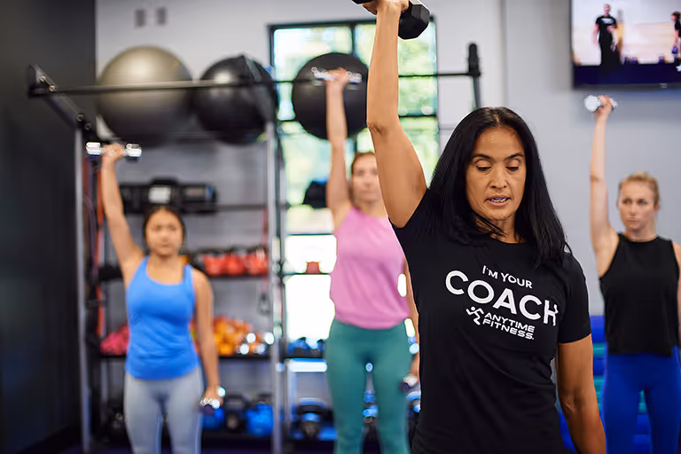 Anytime Fitness coach leading a group strength training class with women lifting dumbbells